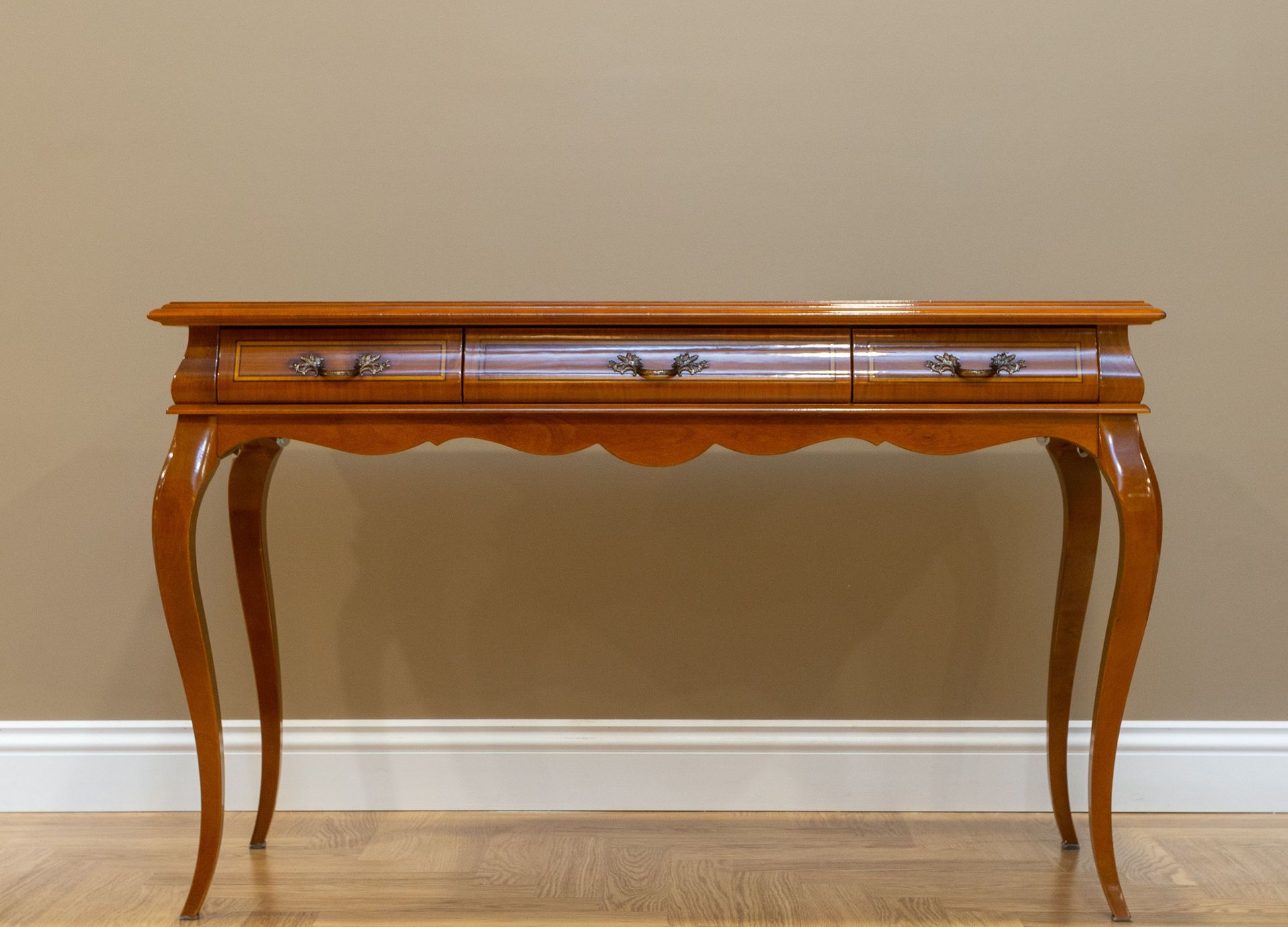 Classic wooden console table with elegant design and metal handles against a beige wall.